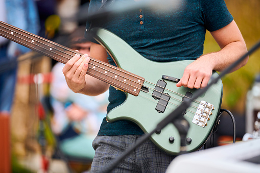 Hands of bassist playing green bass electric guitar on concert stage, selective focus, live music concept. Musician bassist playing melody on bass guitar during performance at concert