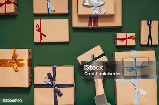 istock Anonymous Person Holding One of Many Gift Boxes on a Green Background 1350065490