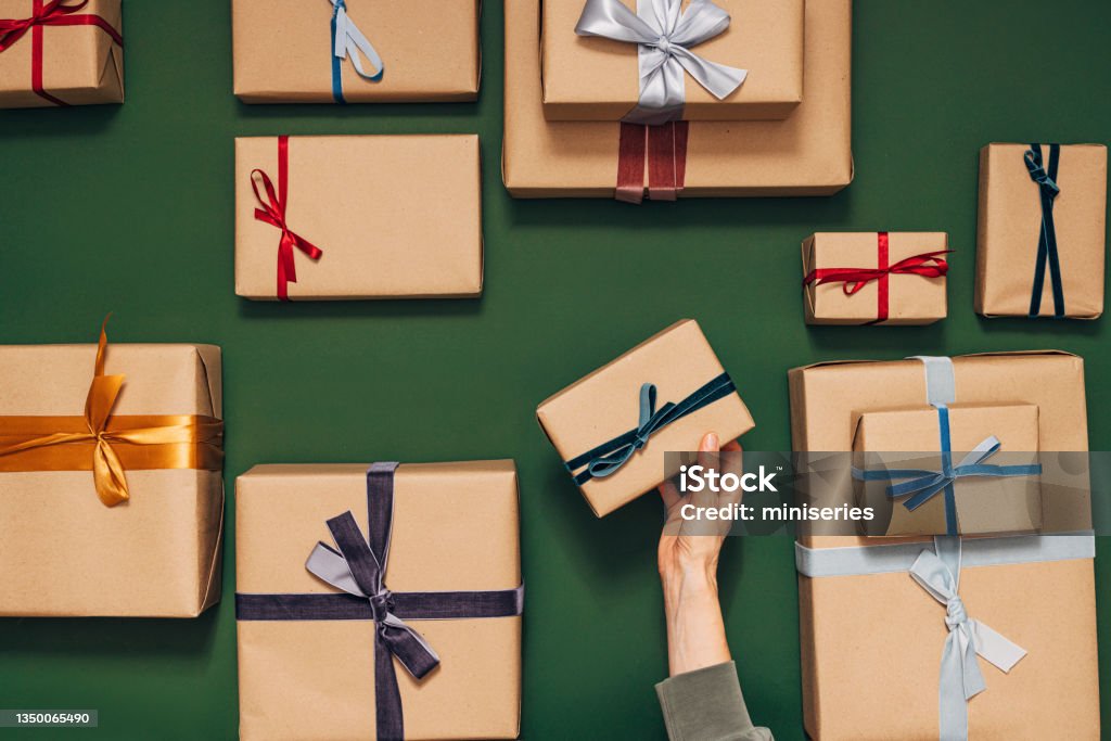 Anonymous Person Holding One of Many Gift Boxes on a Green Background There are many nicely wrapped gifts with different colored ribbons Hands of an anonymous person are putting one gift on the table Gift Stock Photo