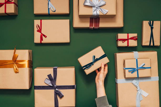 Anonymous Person Holding One of Many Gift Boxes on a Green Background There are many nicely wrapped gifts with different colored ribbons Hands of an anonymous person are putting one gift on the table gift stock pictures, royalty-free photos & images