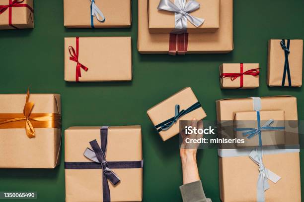 Anonymous Person Holding One Of Many Gift Boxes On A Green Background Stock Photo - Download Image Now