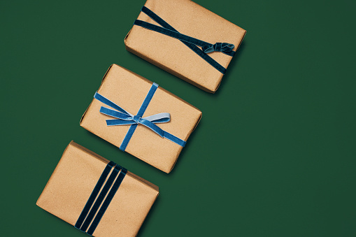 Three beautifully and carefully wrapped Christmas presents laying on a green table and are decorated with different style blue ribbons