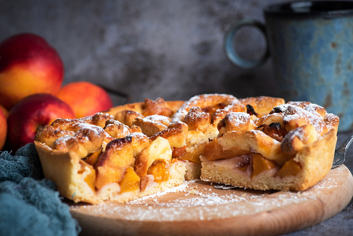 Homemade American pie with peaches on a wooden board with peaches on a gray background. Healthy, tasty, vegetarian food