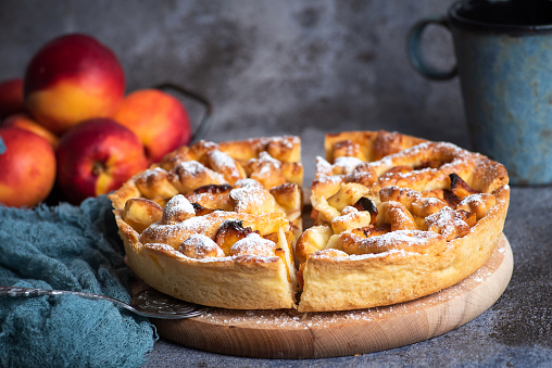 Homemade American pie with peaches on a wooden board with peaches on a gray background. Healthy, tasty, vegetarian food