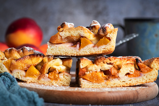 Homemade American pie with peaches on a wooden board with peaches on a gray background. Healthy, tasty, vegetarian food