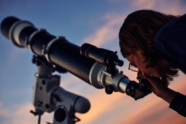 istock Girl with astronomical telescope stargazing under twilight sky. 1350067282