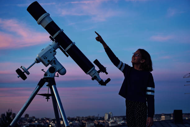 istock Girl with astronomical telescope stargazing under twilight sky. 1350067298
