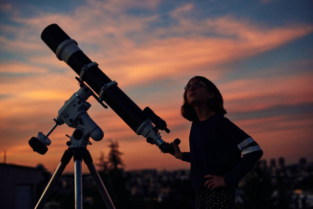 istock Girl with astronomical telescope stargazing under twilight sky. 1350067307