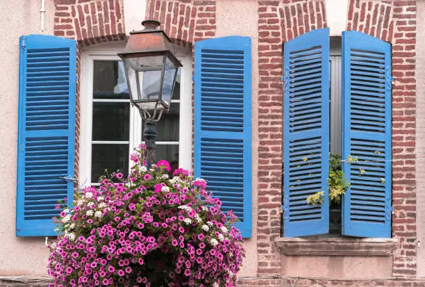 Windows of a french brick house in Honfleur, Normandy, with blue wooden shutters and flower composition