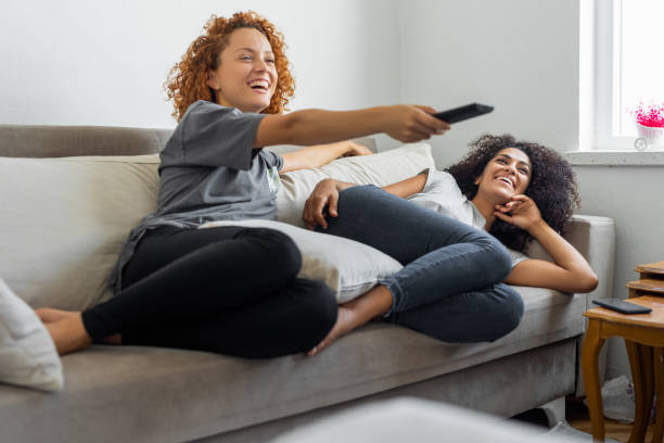 le amiche stanno guardando il loro programma televisivo preferito mentre sono sedute sul divano - guardare la tv foto e immagini stock