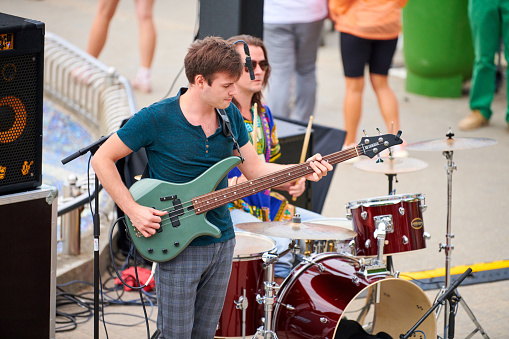 Svetlogorsk, Russia - 08.14.2021 - Bass guitar player on concert stage, live music theme. Skilled musician bassist playing melody on green bass electric guitar at summer music festival outdoor