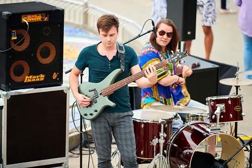 Svetlogorsk, Russia - 08.14.2021 - Bass guitar player on concert stage, live music theme. Skilled musician bassist playing melody on green bass electric guitar at summer music festival outdoor