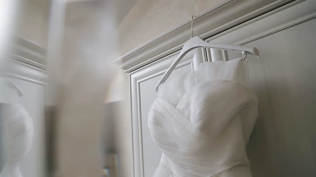 A beautiful white dress is hanging on a hanger on the wall. Close-up of the garment