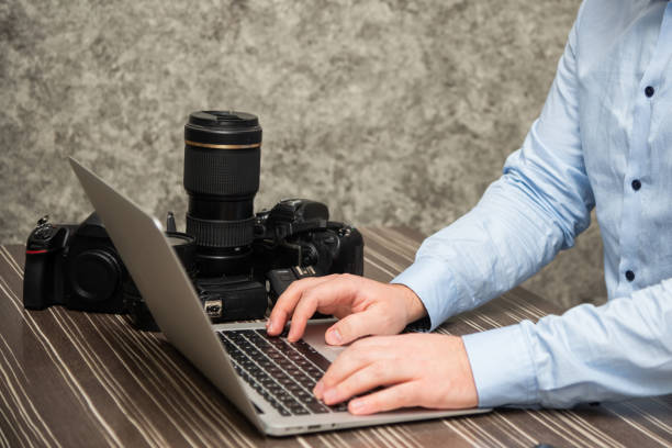 istock Men are working at home on computer, using laptop also. He is a freelance photographer. Photo equipment on the table next to the laptop 1350089105