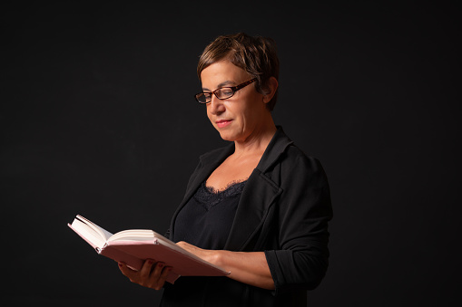 Mature woman is reading a paper book in a black background.