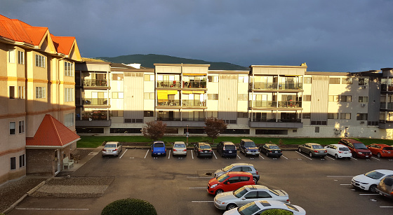 Back of two large three and four storey apartment buildings and a parking lot with cars parked. Late afternoon light in Autumn.dark sky.