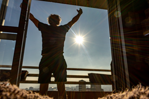 man with arms up on a balcony with arms up on a cloud-cleared day with a sun out