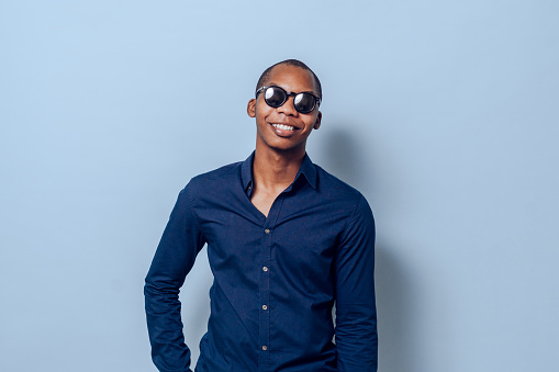 portrait of a cheerful black young man with sunglasses over blue background.