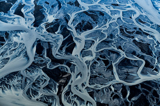 Iceland Braided River Abstract Aerial view from 1500 feet of braided river along southwest coast of Iceland. Braided rivers are usually wide but shallow. They typically form on fairly steep slopes and carry large amount of coarse-grained sediments. When the river’s flow decreases, these sediments get deposited on the river bed leaving behind small temporary islands of sands that cause the river’s channel to split. Aside from a steep gradient and abundance of sediments, a variable water discharge rate is essential to their formation. Consequently, braided rivers exist near mountainous regions, especially those with glaciers. Braided channels are also found in environments that dramatically decrease channel depth, and hence channel velocity, such as river deltas and alluvial fans.    Abstract design is created by different temperatures and densities between glacial feed, spring water and ocean water.  Dark areas indicate fairly translucent spring water.  Light blue areas are glacial water which take on an opaque appearance due to sediments suspended in the water.   Reds are caused by dissolved ferrous iron.  Other dark areas are wet volcanic soil. estuary photos stock pictures, royalty-free photos & images