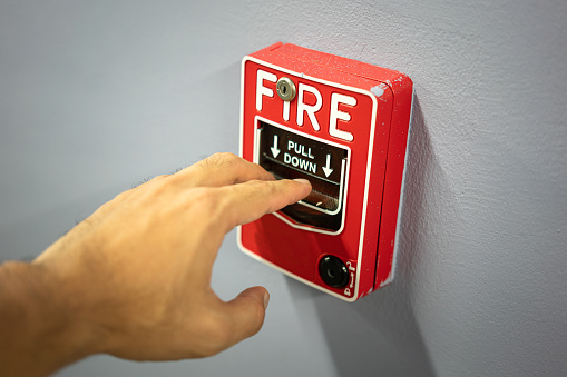 Action of a people hand is activating the emergency fire alarm which is installed on the wall. Emergency evacuation concept photo. Close-up and selective focus at the people finger part.