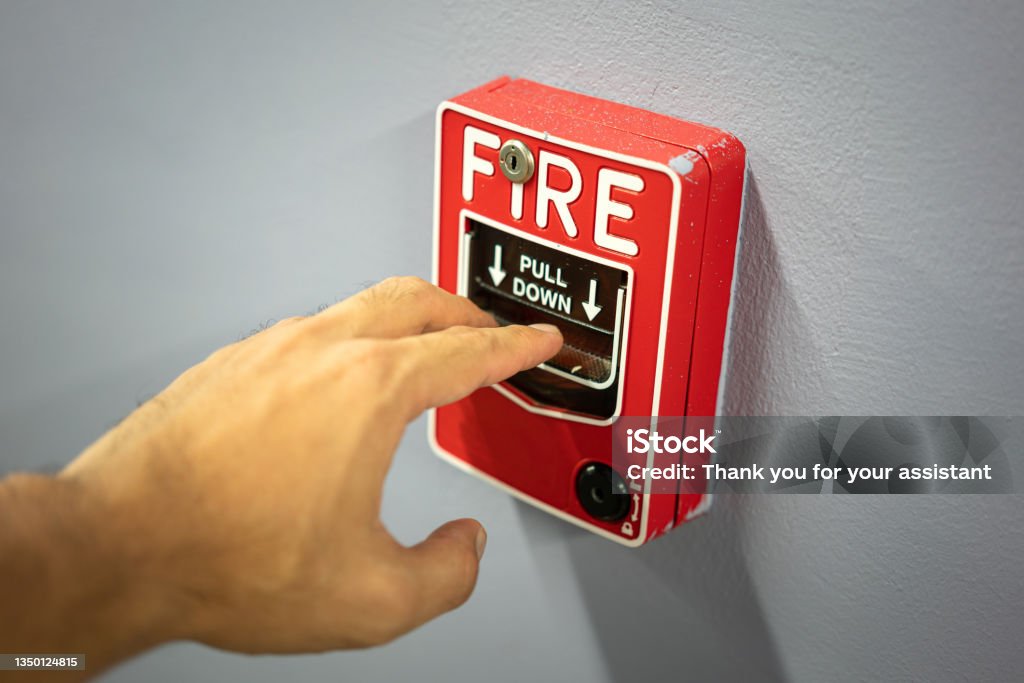 Action of a people  is activating the emergency fire alarm. Action of a people hand is activating the emergency fire alarm which is installed on the wall. Emergency evacuation concept photo. Close-up and selective focus at the people finger part. Fire Alarm Stock Photo