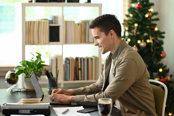istock Side view smiling man working with laptop computer at home. 1350143544