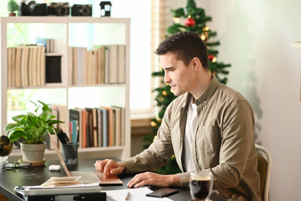 istock Young man sitting in living room and working with computer laptop. 1350143548
