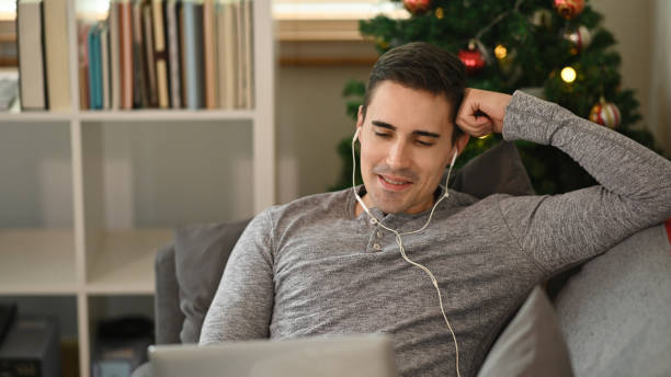 istock Happy young man wearing earphone and using computer laptop on sofa. 1350143576