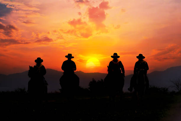 istock Cowboy silhouette on horseback with mountain view and sunset sky. 1350145055