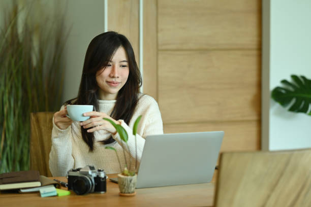 istock Smiling young woman drinking coffee and reading news on laptop computer. 1350145191