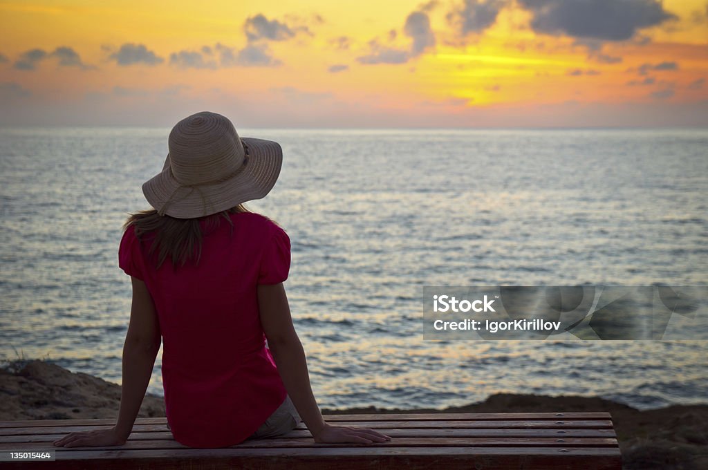 Jeune femme au chapeau assise et à la recherche au coucher du soleil - Photo de 20-24 ans libre de droits