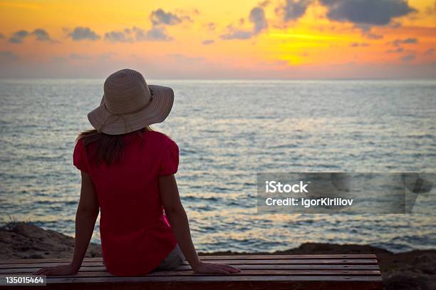 Photo libre de droit de Jeune Femme Au Chapeau Assise Et À La Recherche Au Coucher Du Soleil banque d'images et plus d'images libres de droit de 20-24 ans