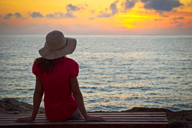 istock Young woman in hat sitting and looking at sunset 135015464