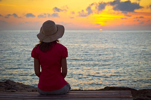 istock Young woman in hat sitting and looking at sunset 135015534