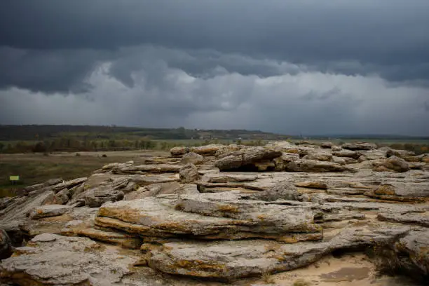 Photo of Huge ancient stones of the Stone Tomb megalith on the ground against the background of storm clouds and fields