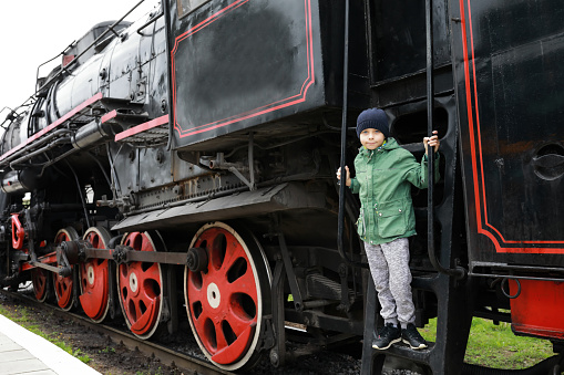 Kid on step of steam locomotive at railway station