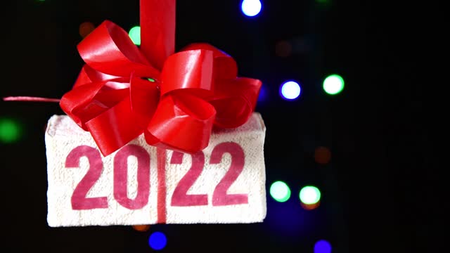 Xmas gift box with text 2022 rotating on black background, new year card, bokeh, selective focus