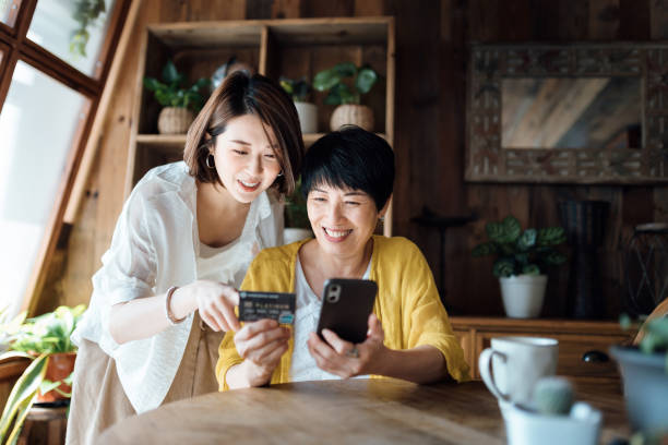 Joyful Asian senior mother and daughter shopping online with smartphone together and making payment with credit card at home Joyful Asian senior mother and daughter shopping online with smartphone together and making payment with credit card at home asian daughter stock pictures, royalty-free photos & images