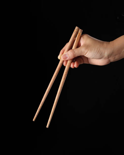 istock Hand holding chopsticks isolated on black background 1350165186