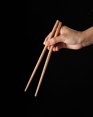 Hand holding chopsticks isolated on black background