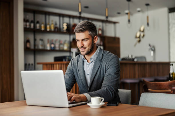 A bearded businessman is sitting in a working friendly cafe and working on an important project. A businessman is typing on the laptop. A businessman using laptop in cafe stock photo