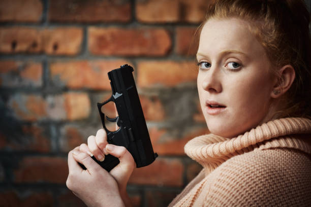 銃を持ち、カメラに驚き、不安そうに見える若い赤毛の女性 - gun women semi automatic pistol young women ストックフォトと画像