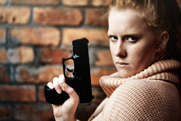 Young woman with red hair holding a semiautomatic pistol against a bare brick wall.