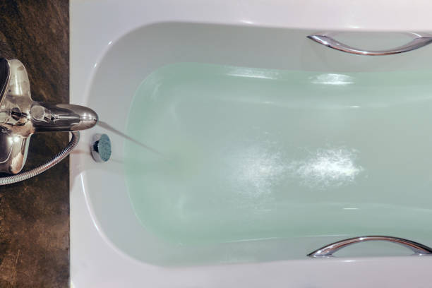 The white bath is filled from the tap with water, close-up