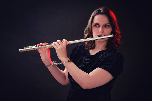 istock Woman musician with a flute in handcuffed hands on a studio dark background. Problems of musical playing at concerts, the concept of non-freedom and arrests 1350178092