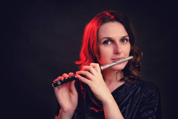 Portrait of a woman musician with a piccolo flute on a studio black background. Flutist with a small flute in her hands Portrait of a woman musician with a piccolo flute on a studio black background. Flutist with a small flute in her hands piccolo stock pictures, royalty-free photos & images