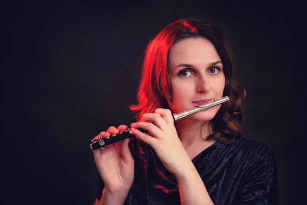 Portrait of a woman musician with a piccolo flute on a studio black background. Flutist with a small flute in her hands