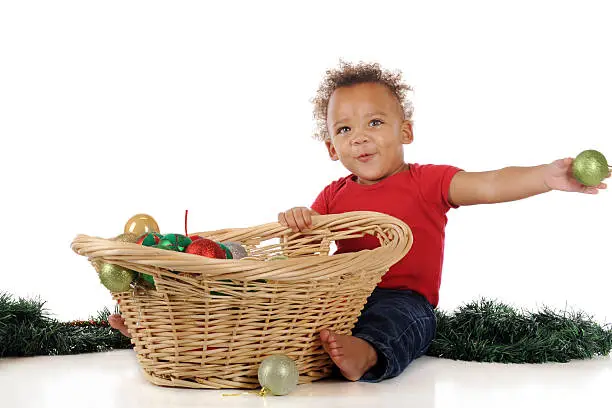 A handsome toddler boy tossing bulbs from a basket full of Christmas ornaments.  On a white background.