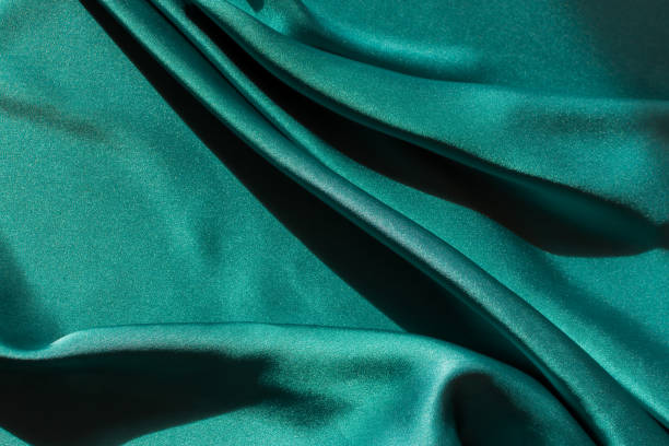 istock Blue-green satin fabric. Smooth silk fabric cut off on the table. 1350180841