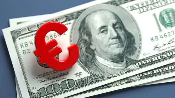 Red-colored Euro symbol and American hundred dollar bill. On grayish blue-colored background. Horizontal composition with copy space. Focused image.